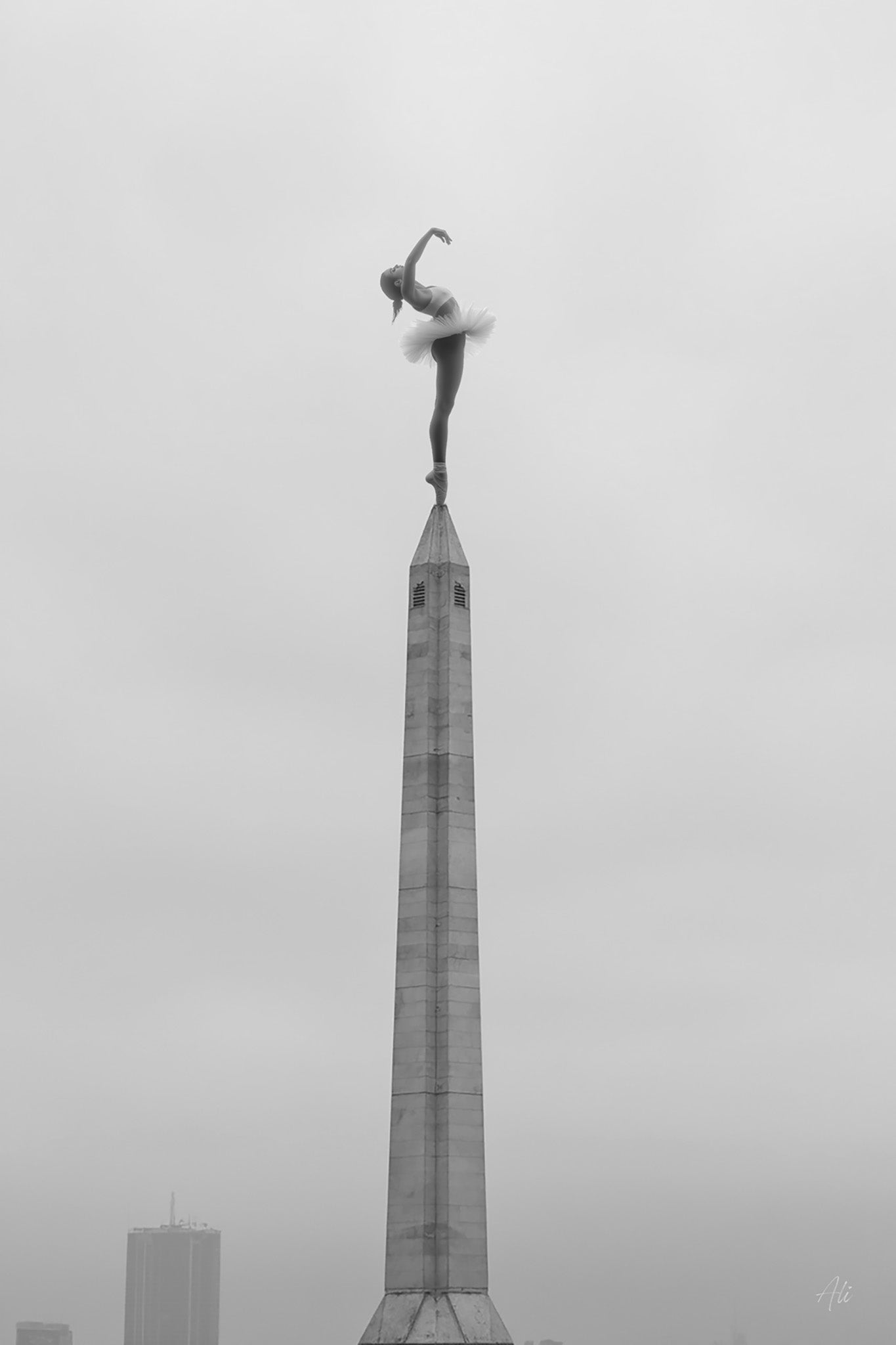 Black and white fine art ai photograph of a ballerina in a dramatic arched back pose on the tip of a tall spire, viewed from below, with high contrast and ethereal lighting accentuating her silhouette against the sky.