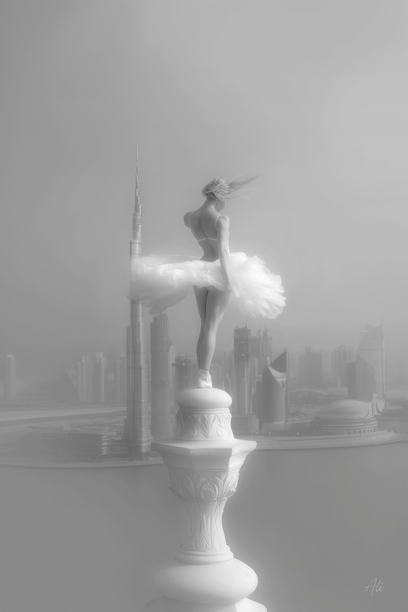 Black and white fine art photograph of a ballerina posed as an ethereal angel, balancing atop a Dubai spire with windswept hair, overlooking the Dubai Water Canal and the city's futuristic skyline, captured with dreamy contrast and soft lighting.