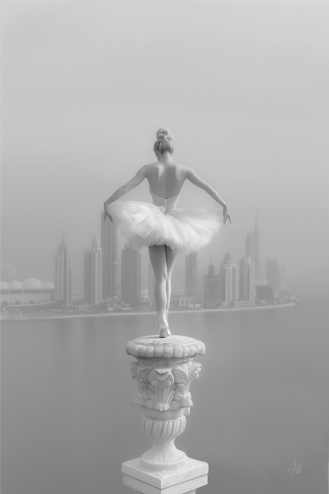 Black and white fine art photograph of a glowing ballerina in an hourglass pose, balanced atop a Dubai spire with the Dubai Water Canal and the city's futuristic skyline visible in the background, captured with high contrast and ethereal lighting.