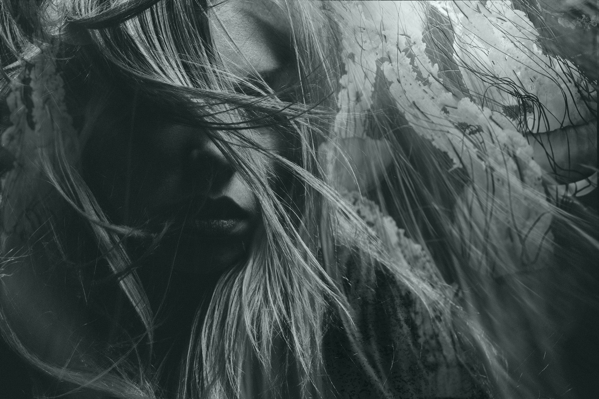 Monochrome portrait of a mysterious woman with hair over her face, showcasing emotion and dramatic lighting in a blurred, moody style.