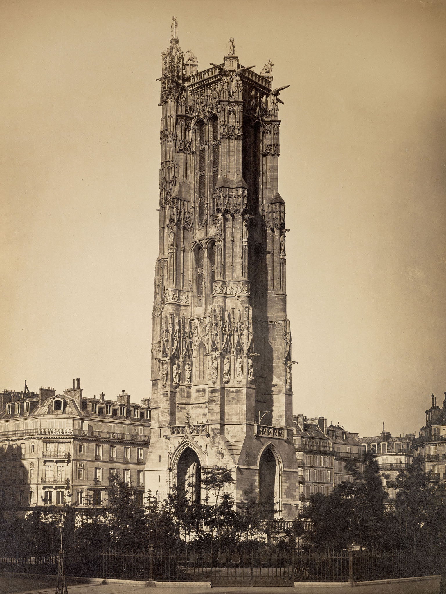 Sepia-toned photograph of "The Tour St. Jacques," featuring the Gothic architecture of the 16th-century Parisian landmark, with detailed stonework and a cityscape backdrop.