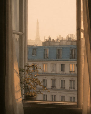 Watercolor illustration of a view through an open French window with sheer curtains and a small potted plant on the sill, looking out over classic Parisian Haussmann-style apartment buildings with blue-grey mansard roofs and warmly lit windows, the Eiffel Tower rising softly in a golden hazy sky in the background.
