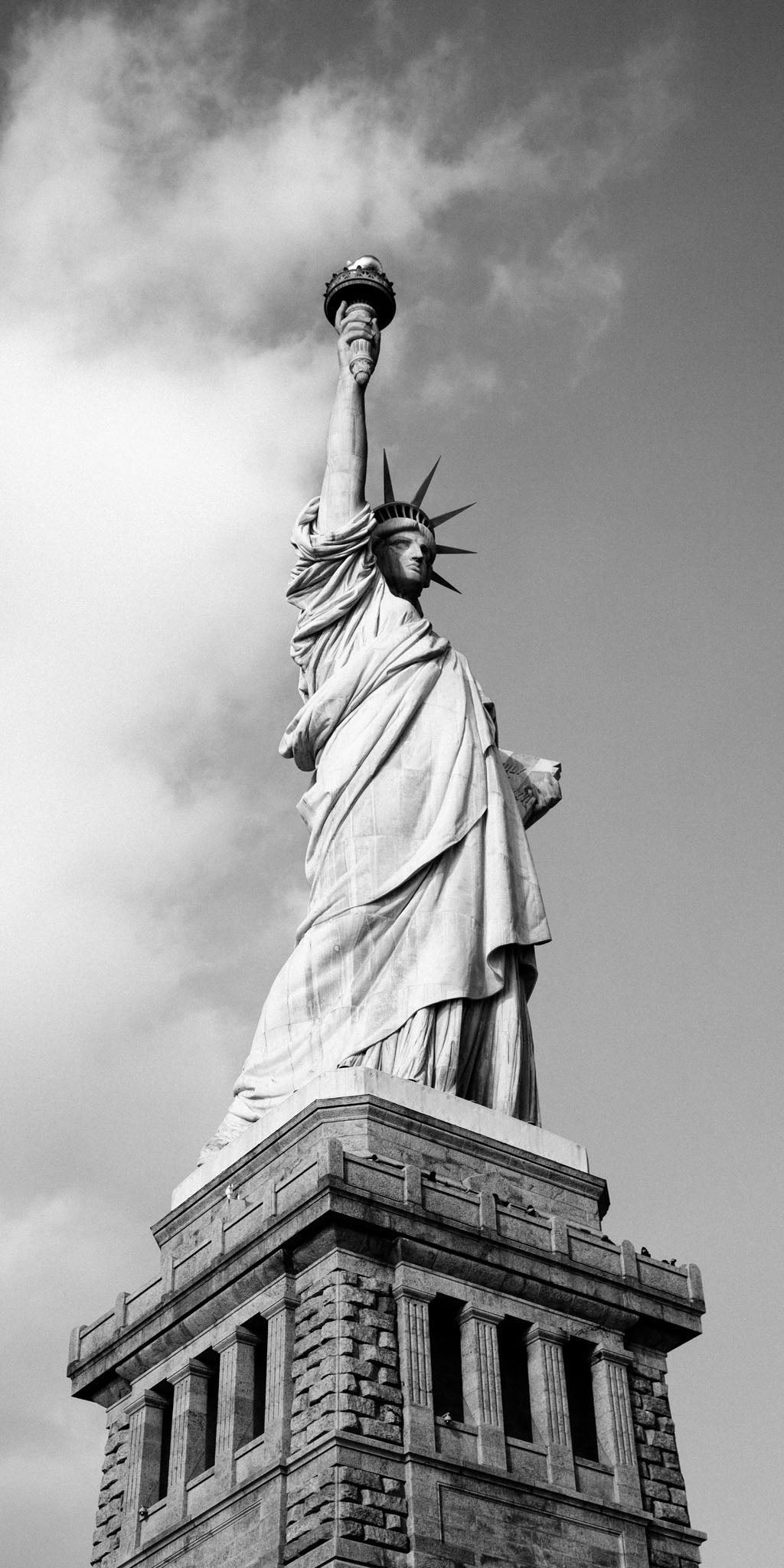 Black and white photograph of the Statue of Liberty, showcasing its iconic design against a serene sky, emphasizing its role as a symbol of freedom and Americana in vintage style.