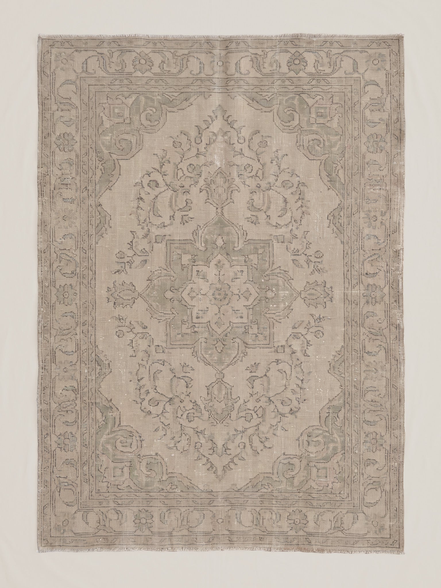 Fine art print of a heavily faded and aged Persian or Turkish-style area rug featuring a central floral medallion, arabesque scrollwork, botanical detailing, and a repeating vine border, rendered in soft taupes, warm grays, and pale creams with a ghostly, ethereal quality.