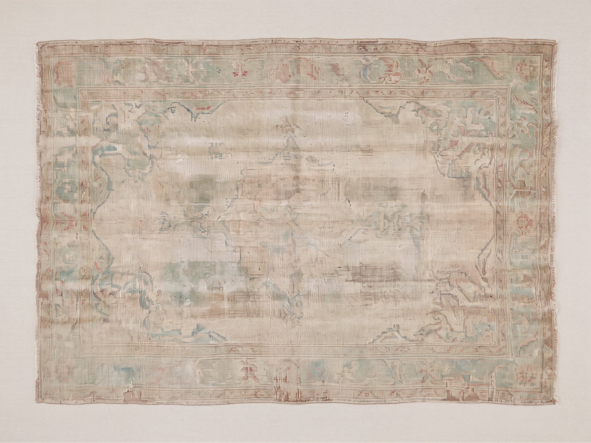 Fine art print of a heavily worn antique Persian or Turkish-style rug featuring a faded medallion and floral arabesque design in soft ivory, pale sage green, dusty rose, and taupe tones, with visible fringe edges and a formal botanical border.