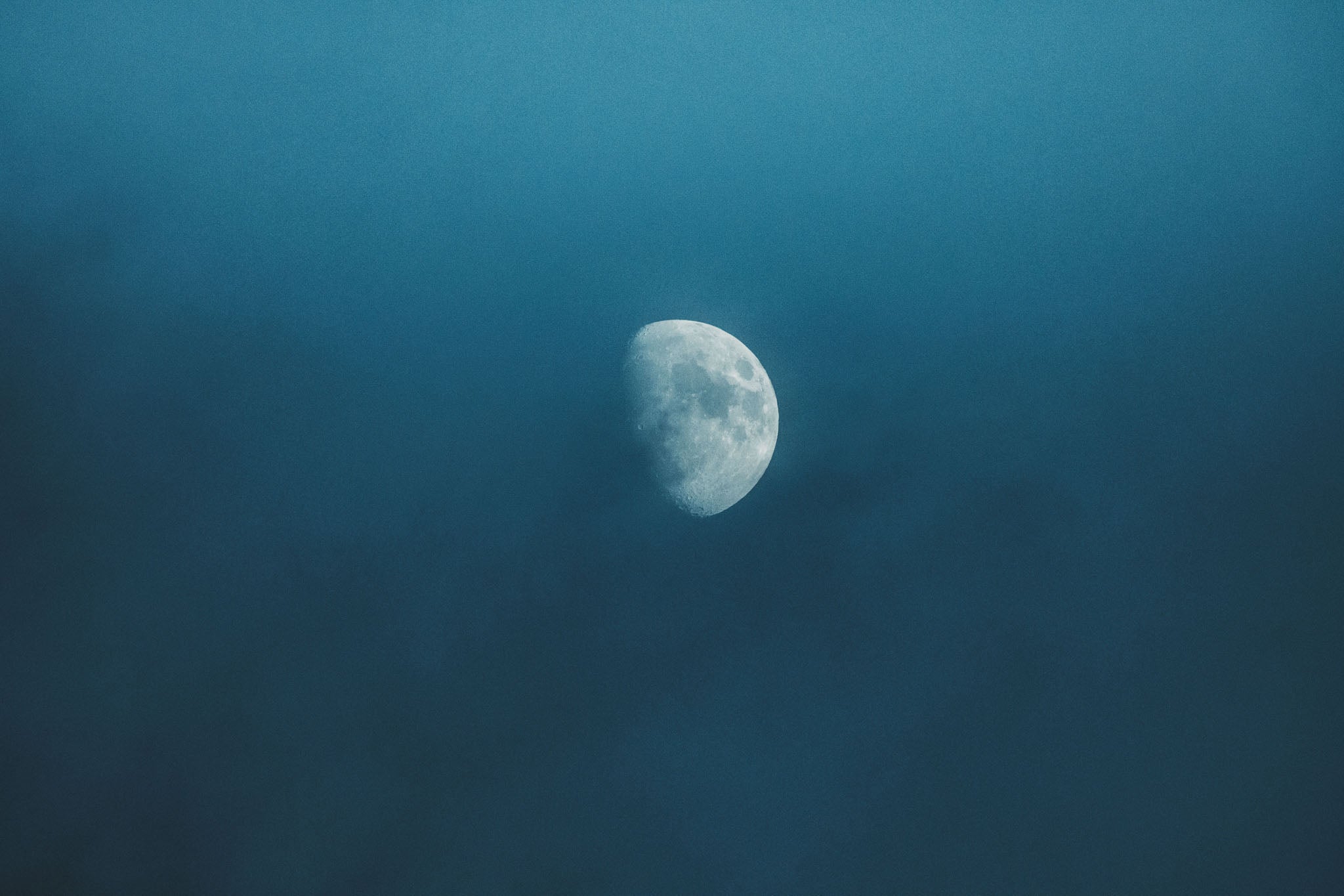 Photography of a waning gibbous moon against a tranquil night sky, featuring a soft blue and white gradient that highlights the lunar surface's craters and ethereal beauty.