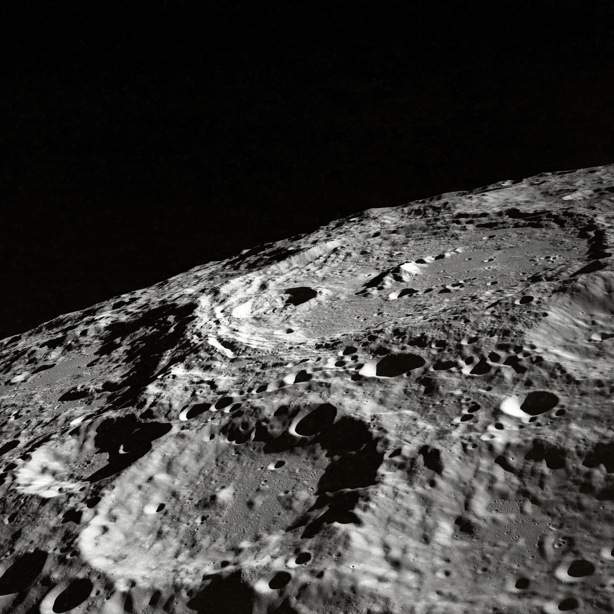 Black and white photograph of the moon's surface, emphasizing detailed craters and barren regolith, with a focus on the impact marks and cosmic tranquility.