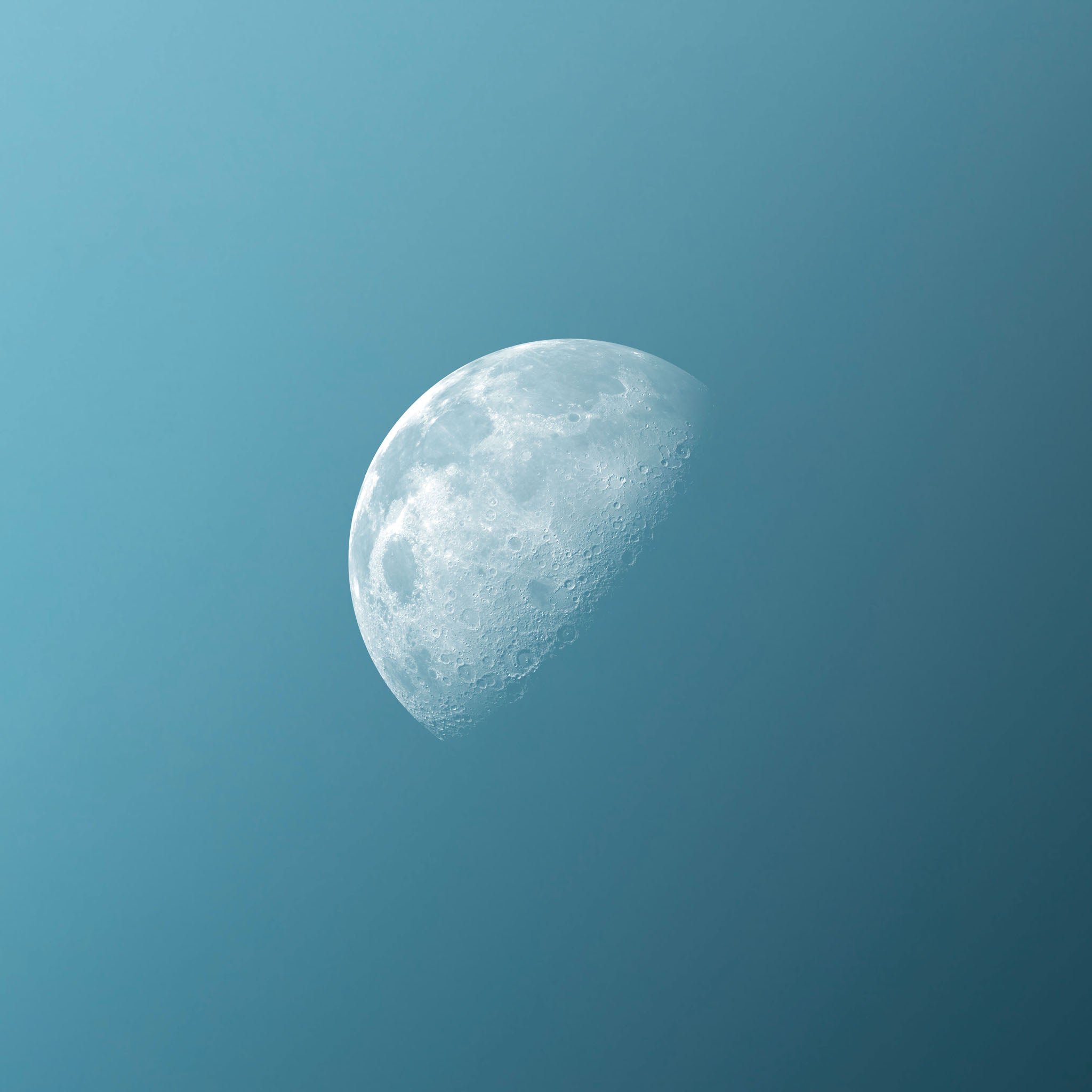 Photograph of the moon’s cratered surface in blue and white, set against a teal background, showcasing the waxing gibbous phase with a serene and surreal cosmic atmosphere.